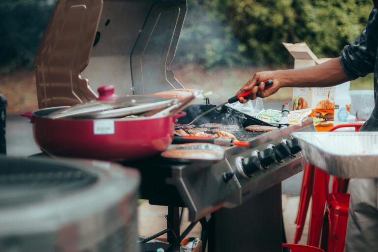 A close-up of grilling meats on a barbecue with visible smoke outdoors.