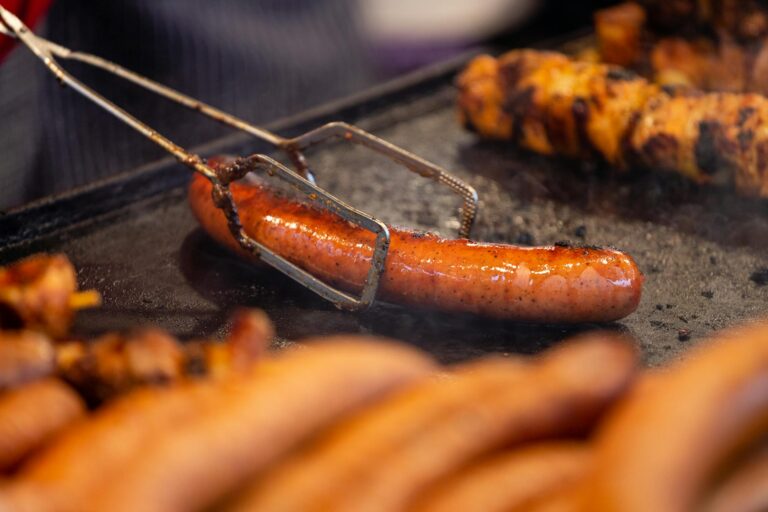 A juicy sausage being expertly grilled on a barbecue, held with tongs. Perfect for BBQ enthusiasts.