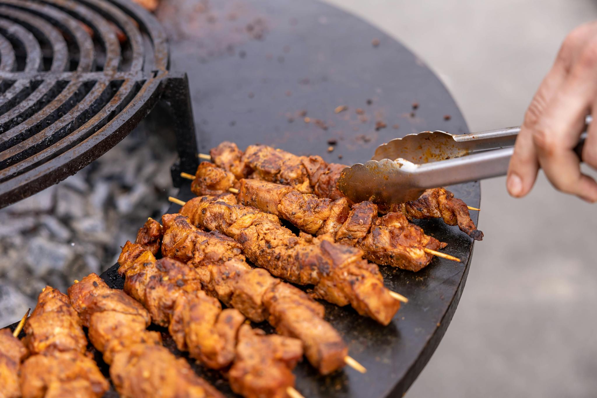 Close-up of meat skewers grilling outdoors, highlighting texture and flavor.